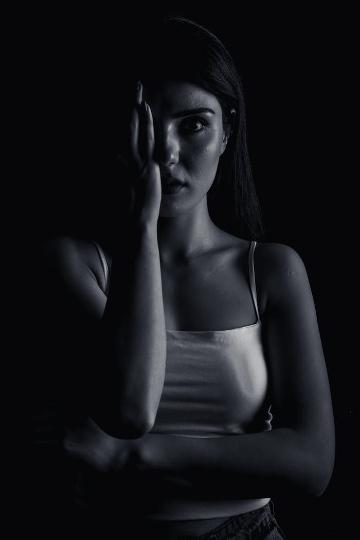 Moody black and white portrait of a woman partially covering her face in a dark setting.